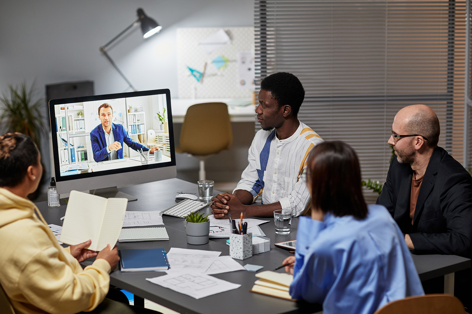 Diverse business team listening to man on computer screen during online meeting in office